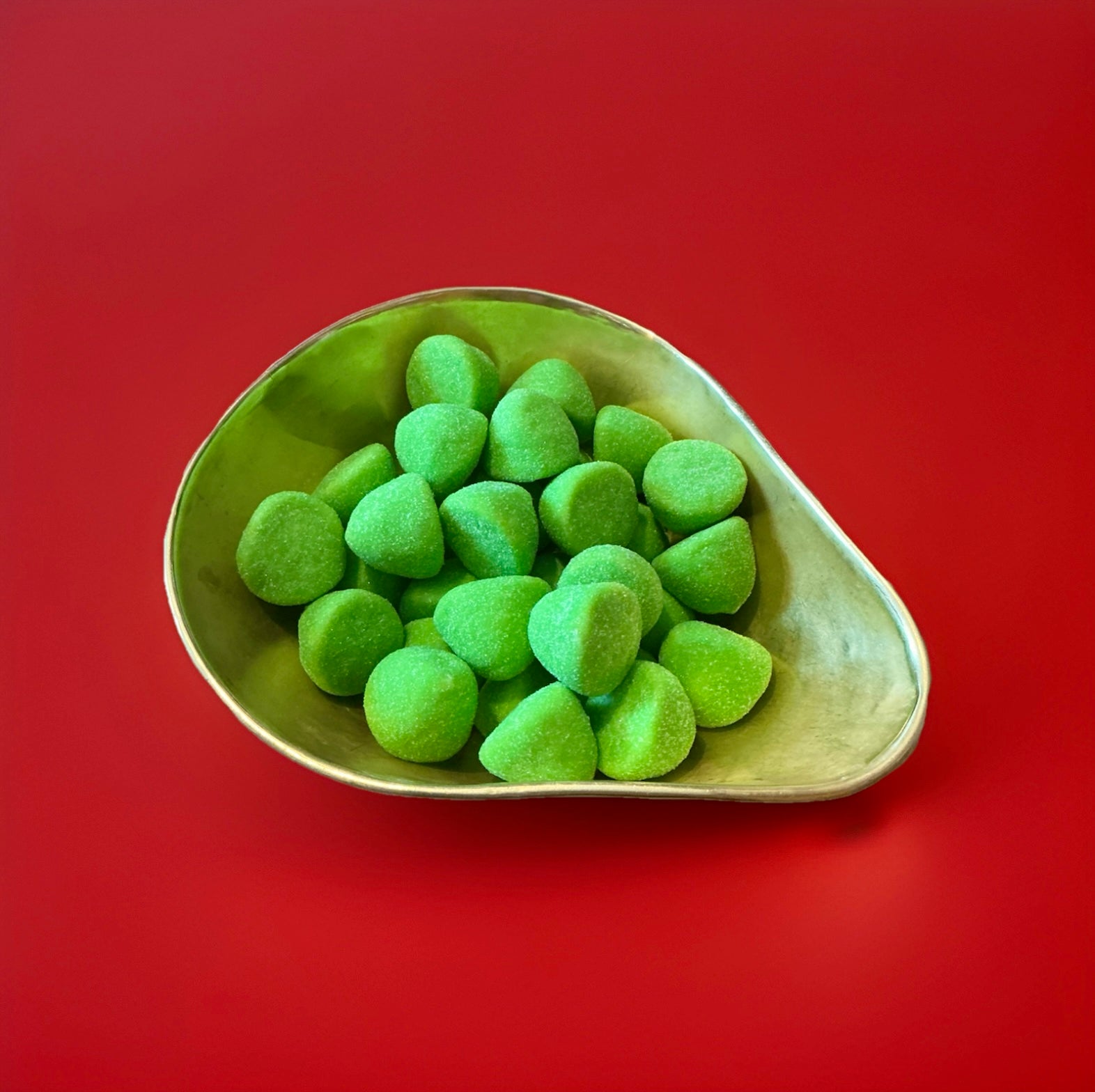 Large bright green marshmallows coated in sugar in a gold bowl with a red background 