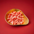 Red coloured oval shaped hard boiled sweets with a sarsaparilla flavour and a sugar coating in a gold bowl with a red background 