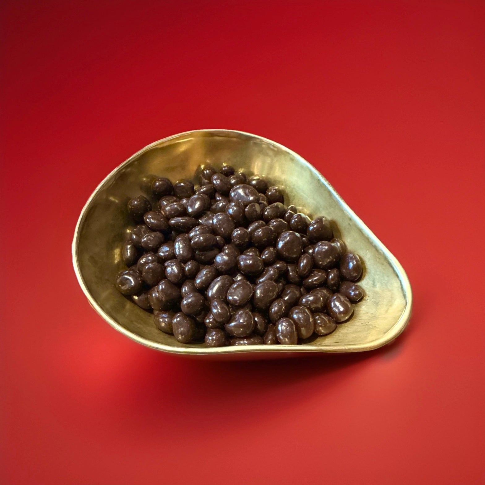 Carol Anne dark chocolate coated cranberries in a gold bowl with a red background 