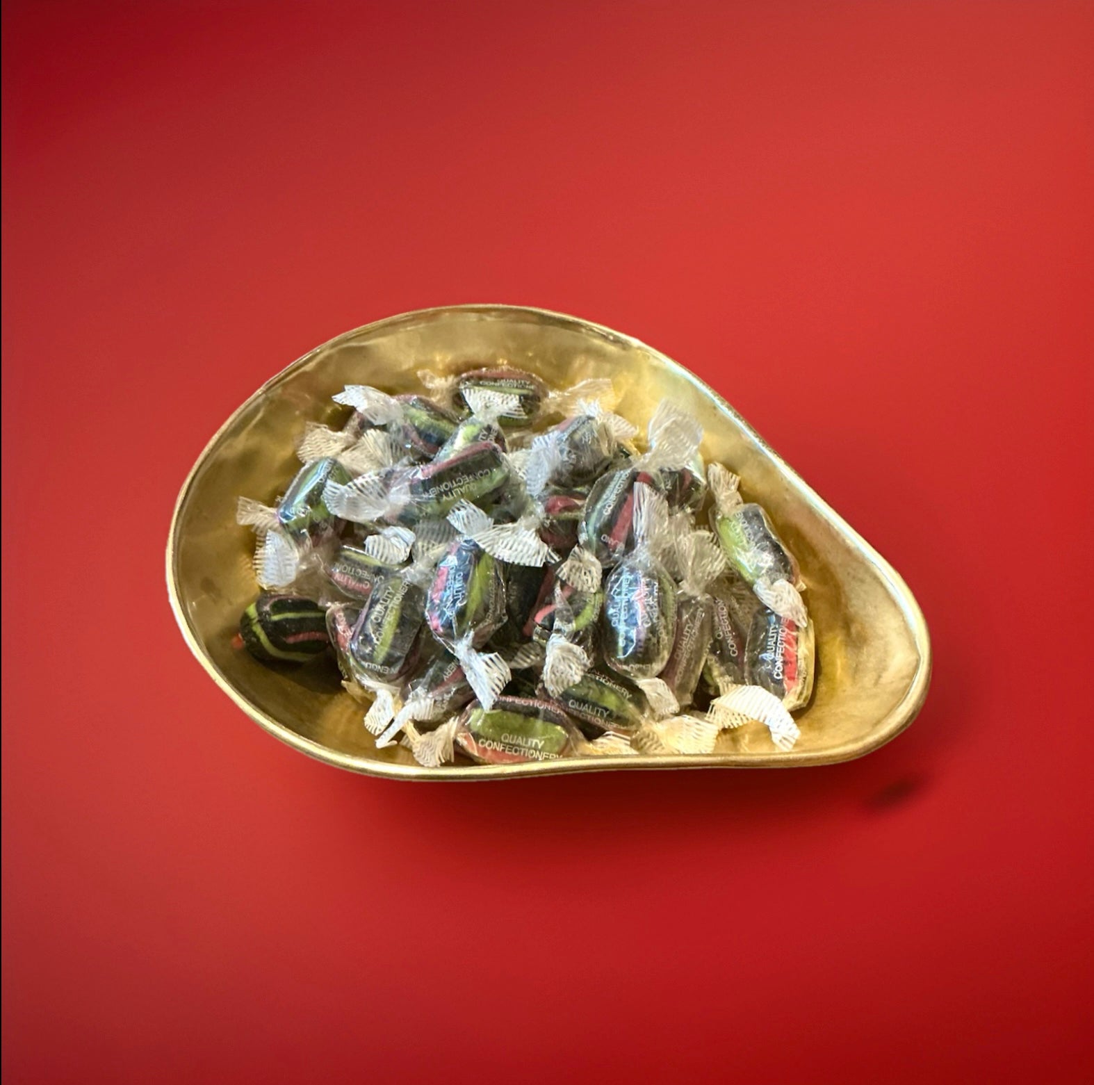 Individually wrapped black pink and green striped hard boiled liquorice and aniseed flavoured sweets in a gold bowl on a red background 