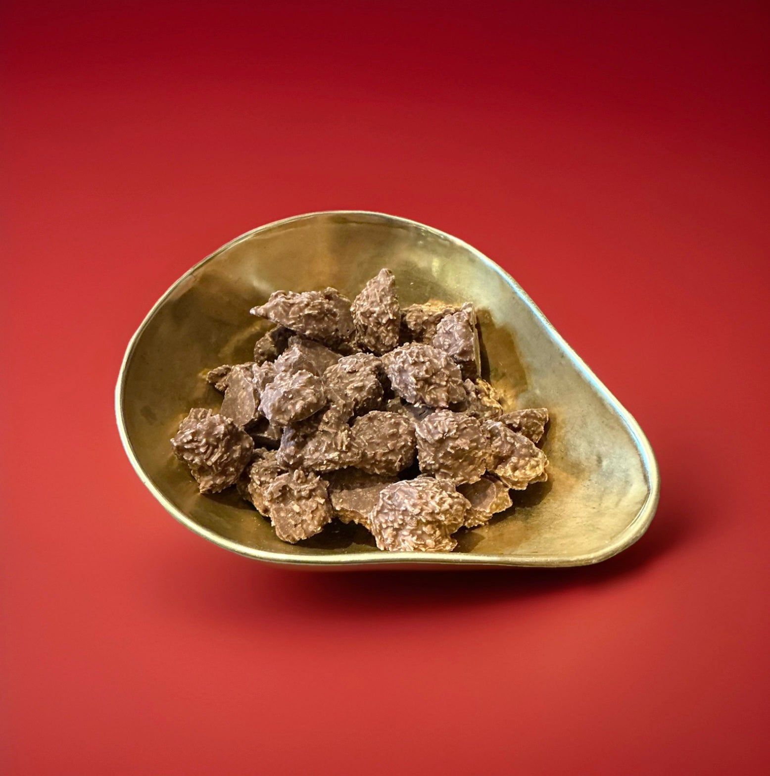 Milk chocolate covered coconut macaroon clusters in a gold bowl on a red background 