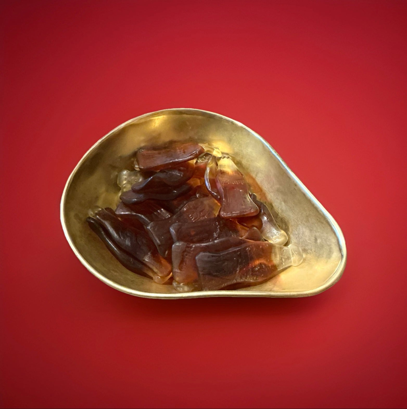 Giant cola bottle jelly sweets in a gold bowl on a red background 