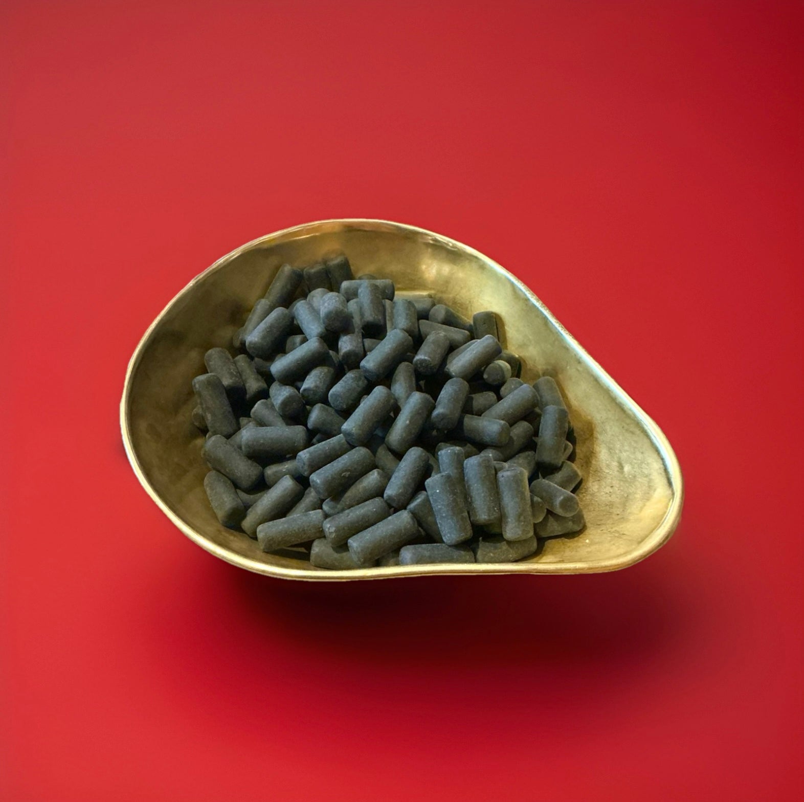 Black coloured crispy outer liquorice flavoured outer shell with a black liquorice centre in a gold bowl on a red background 