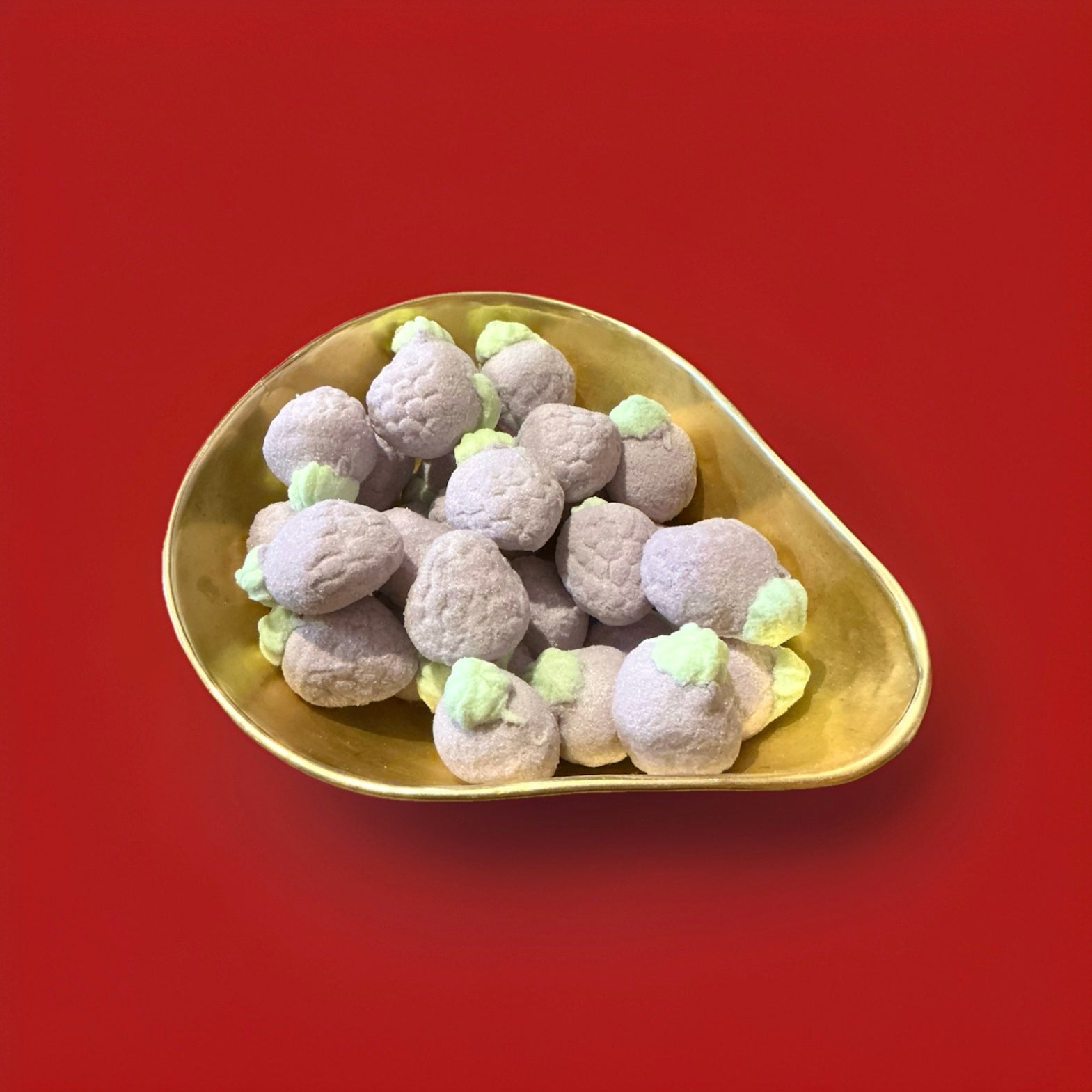 Large purple and green blackberry flavoured marshmallows with a jelly centre in a gold bowl with a red background 