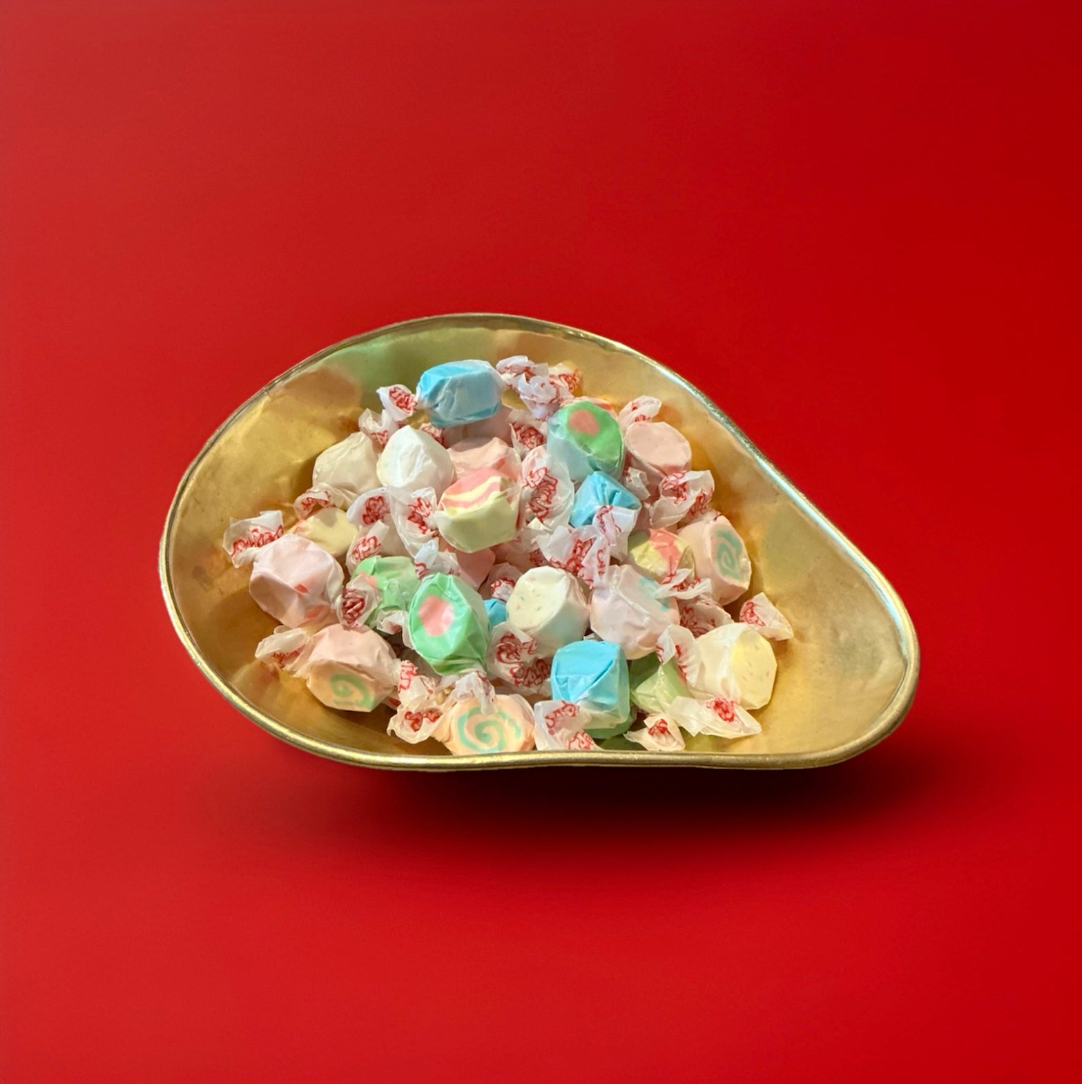 mixed flavours of salt water taffy in a gold bowl with a red background 