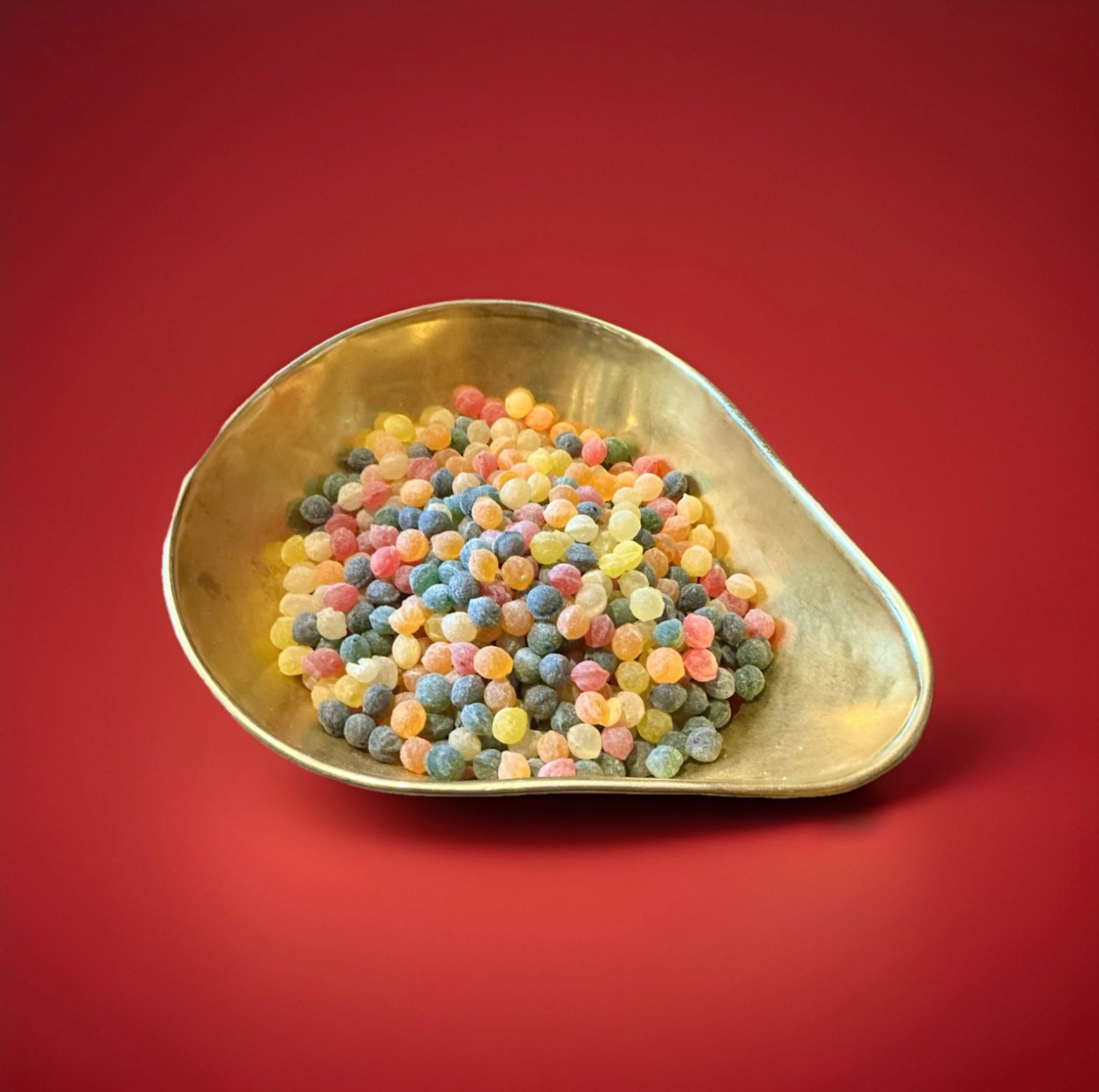 Hard boiled mixed fruit flavoured pips in a gold bowl on a red background 