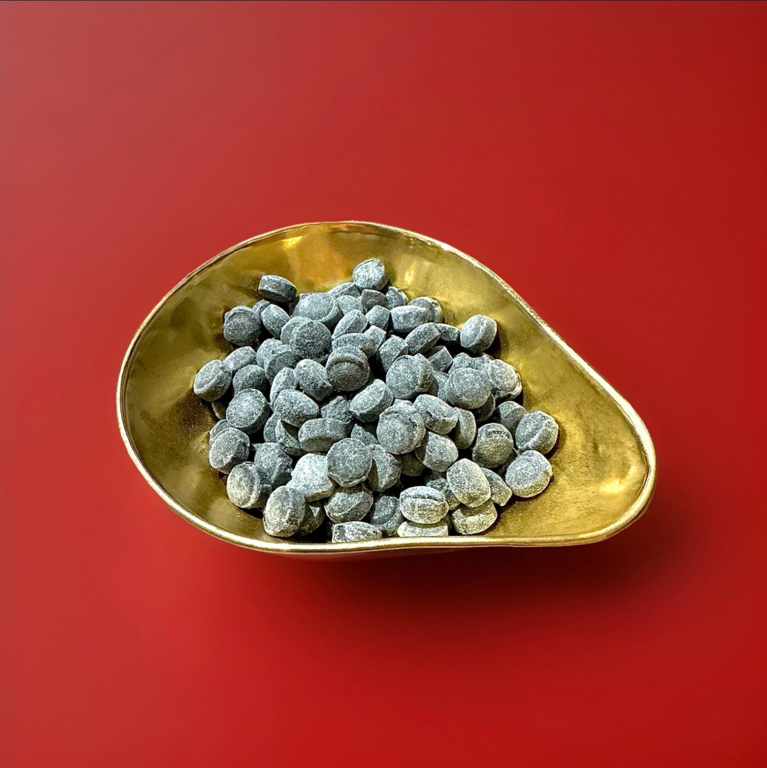 Liquorice and aniseed flavoured black hard boiled sweets n a gold bowl on a red background 