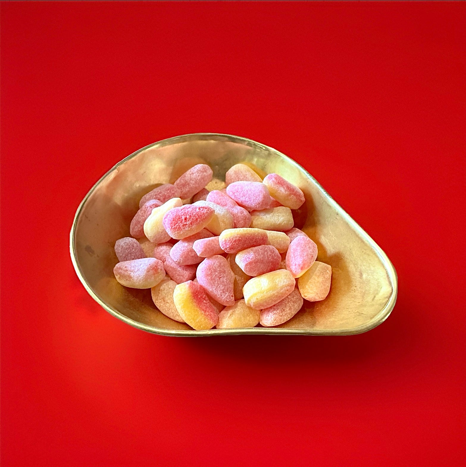 Large hard boiled pear drops in a gold bowl on a red background 