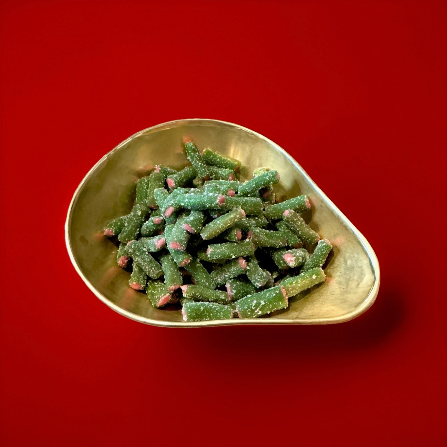 Green and pink liquorice and fondant tubes with a sour sugar coating in a gold bowl with a red background 