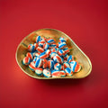 Blue red and white striped oval shaped cream soda flavoured soft rock sweets in a gold bowl on a red background 