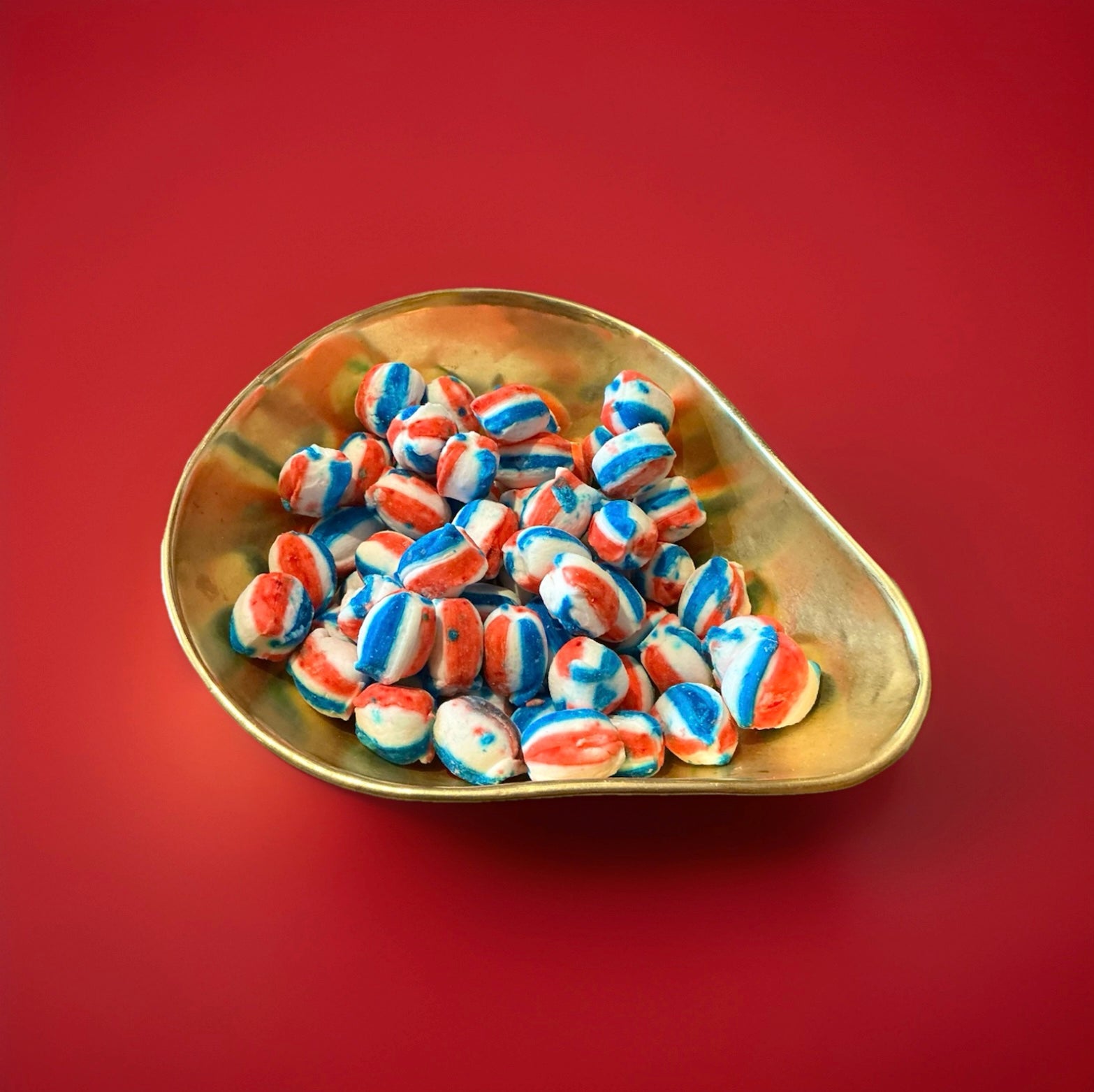 Blue red and white striped oval shaped cream soda flavoured soft rock sweets in a gold bowl on a red background 