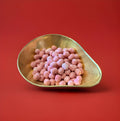 Round shaped pink coloured cherry flavoured Bon Bon’s in a gold bowl on a red background 