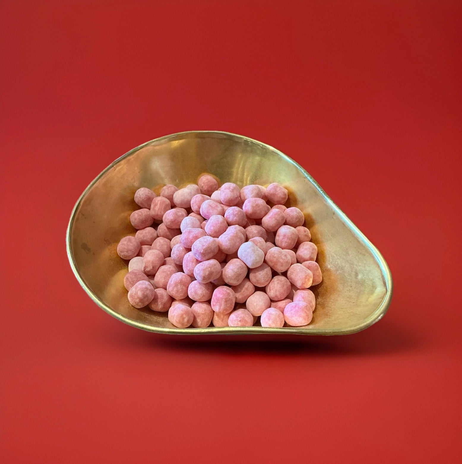 Round shaped pink coloured cherry flavoured Bon Bon’s in a gold bowl on a red background 