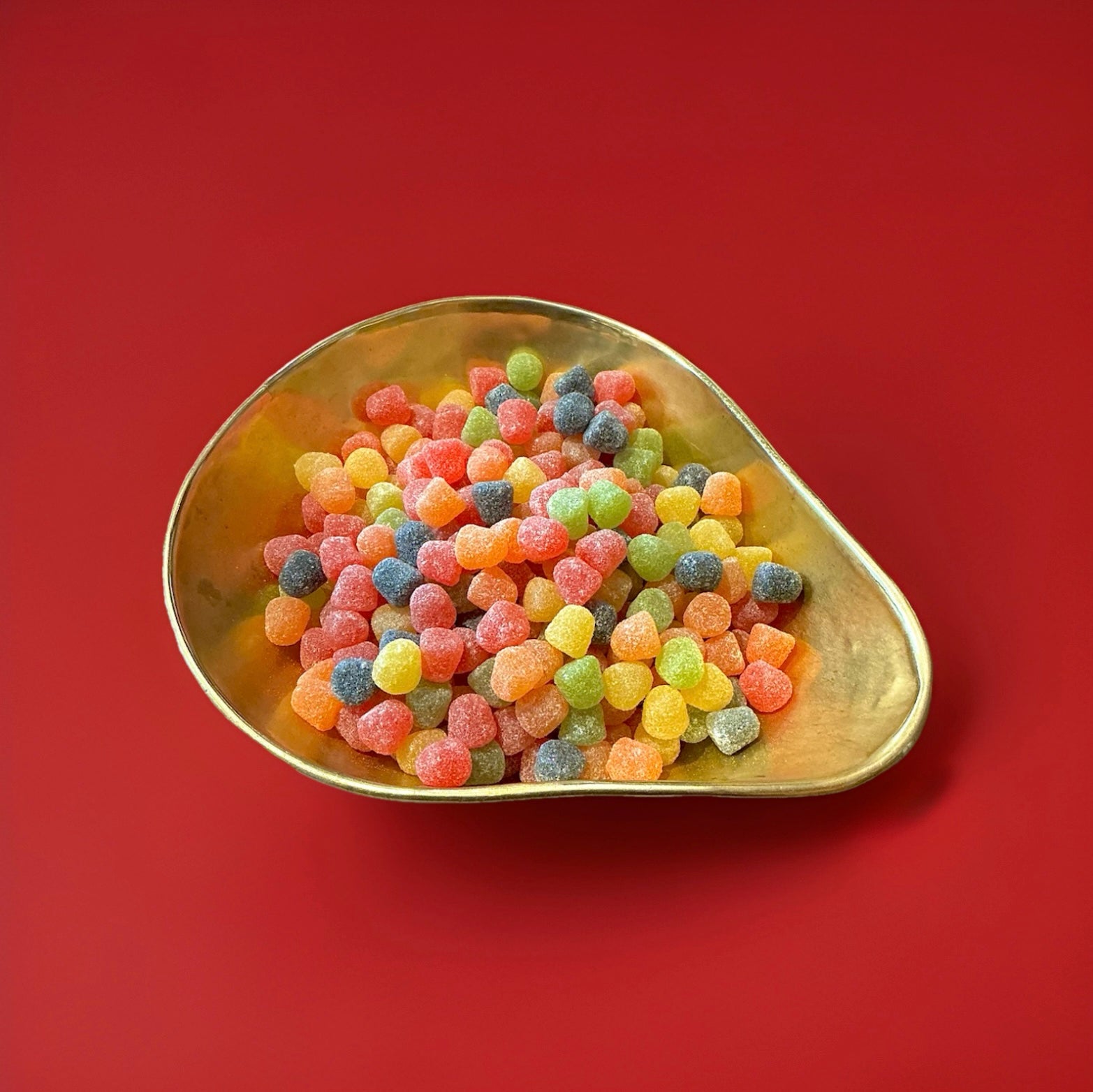 Multicoloured fruit flavoured dew drop sweets with a sugar coating in a gold bowl on a red background 