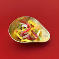 Meerkat shaped mixed fruit jelly sweets in a gold bowl on a red background 