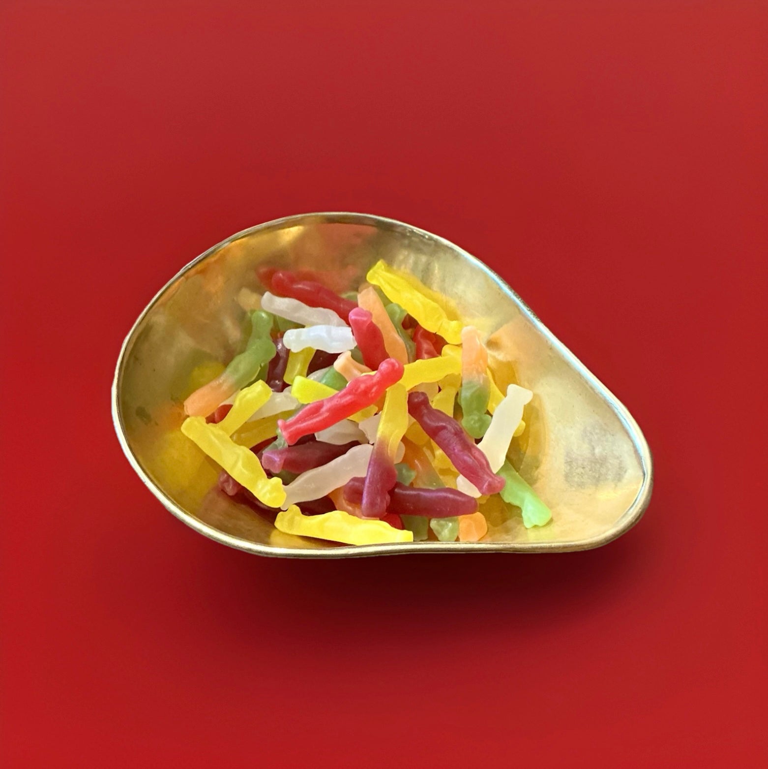Meerkat shaped mixed fruit jelly sweets in a gold bowl on a red background 
