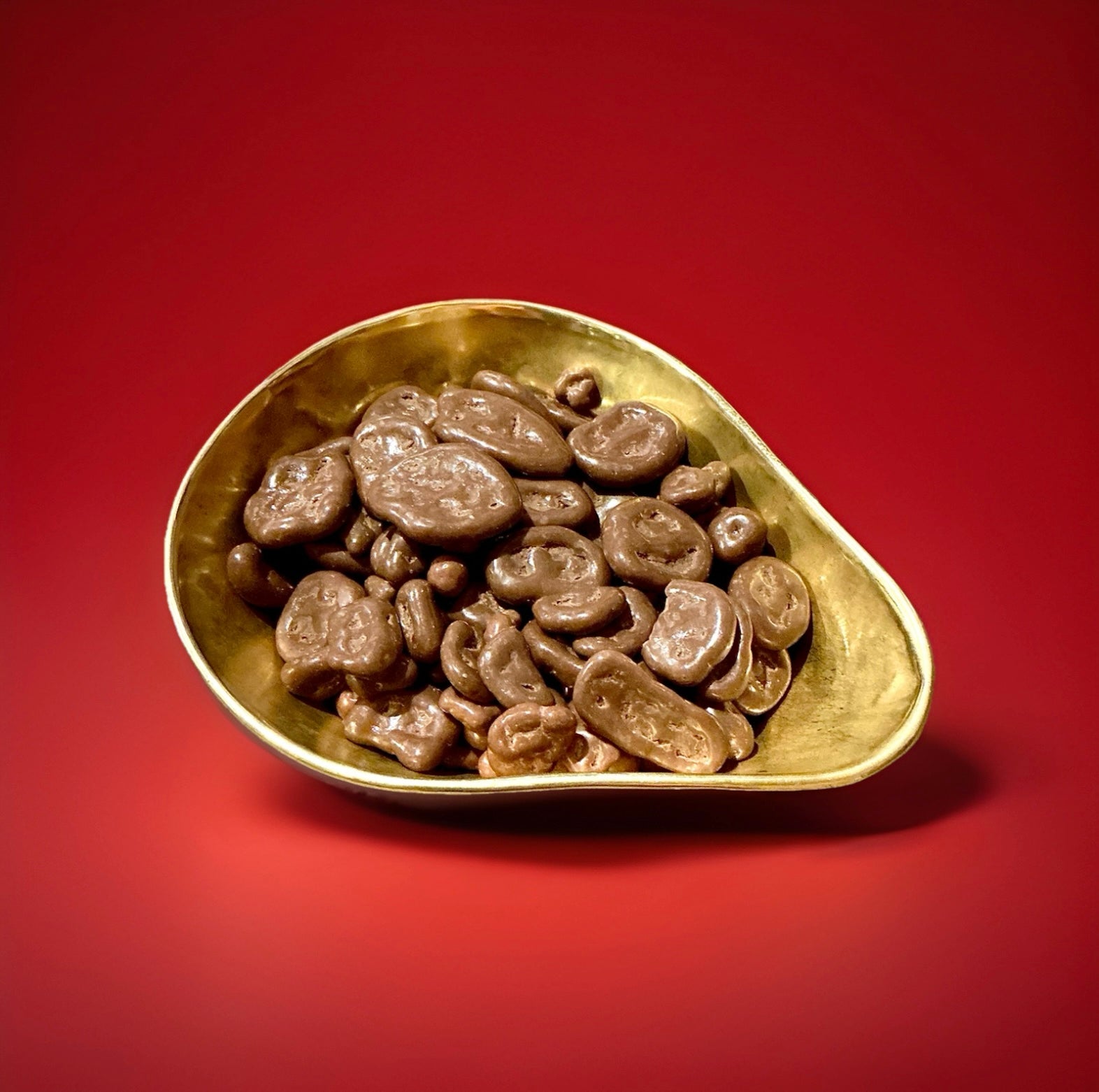Dried banana chips coated in milk chocolate in a gold bowl on a red background 
