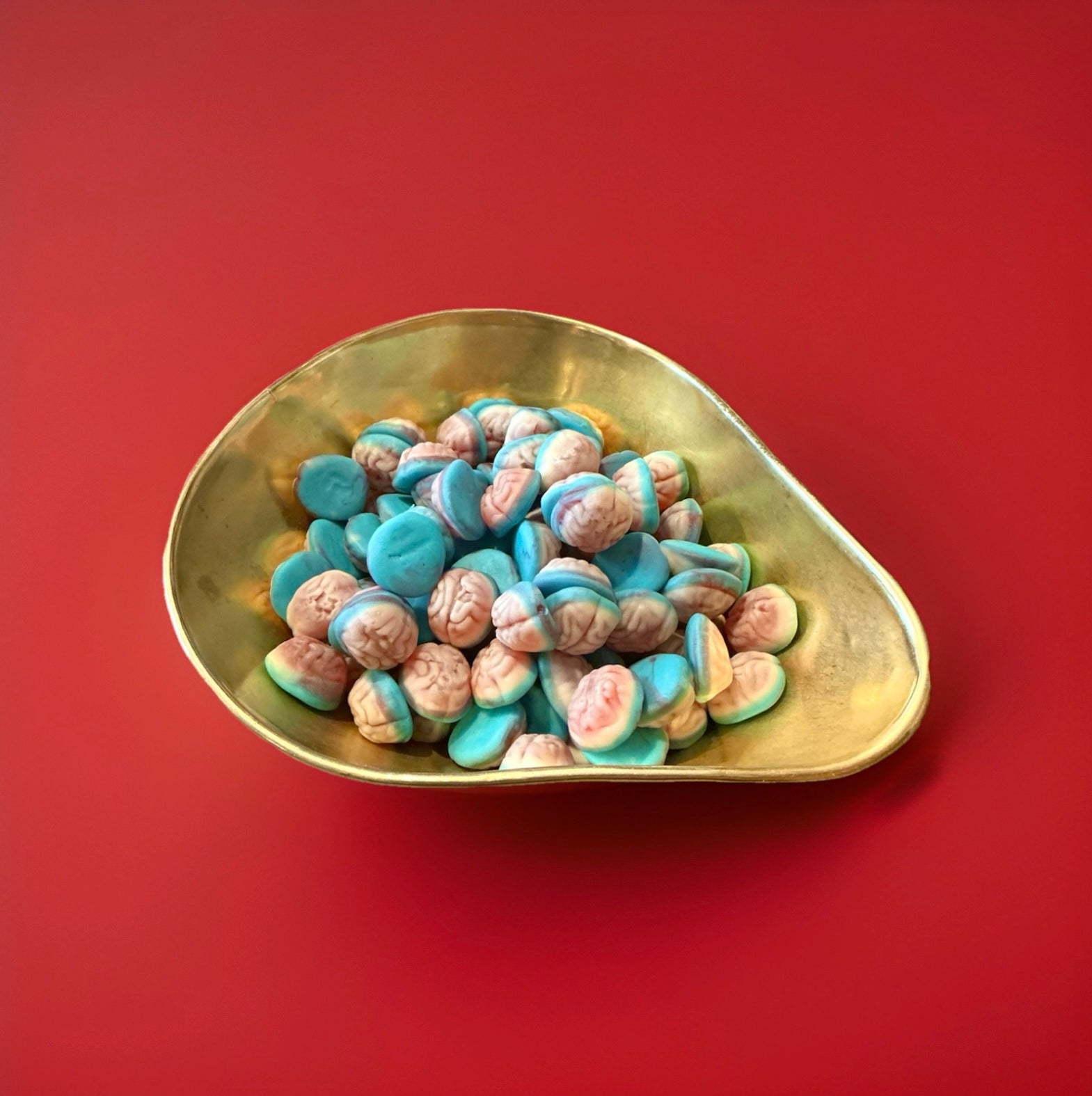 Pink white and blue coloured jelly sweets in the shape of a brain in a gold bowl on a red background 