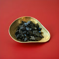 Single salt Dutch black liquorice in the shape of a diamond in a gold bowl on a red background 