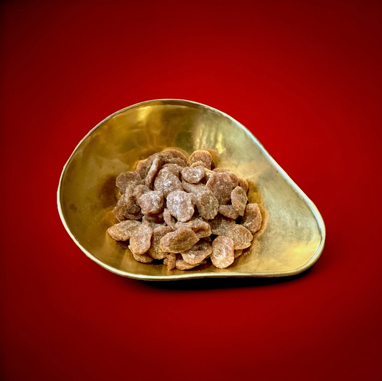 Discs of toffee with a coconut dusting in a gold bowl on a red background 