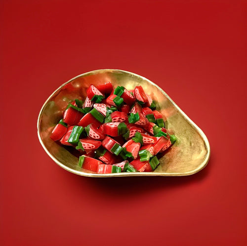 Red and green strawberry shaped sweets in a gold bowl with a red background 