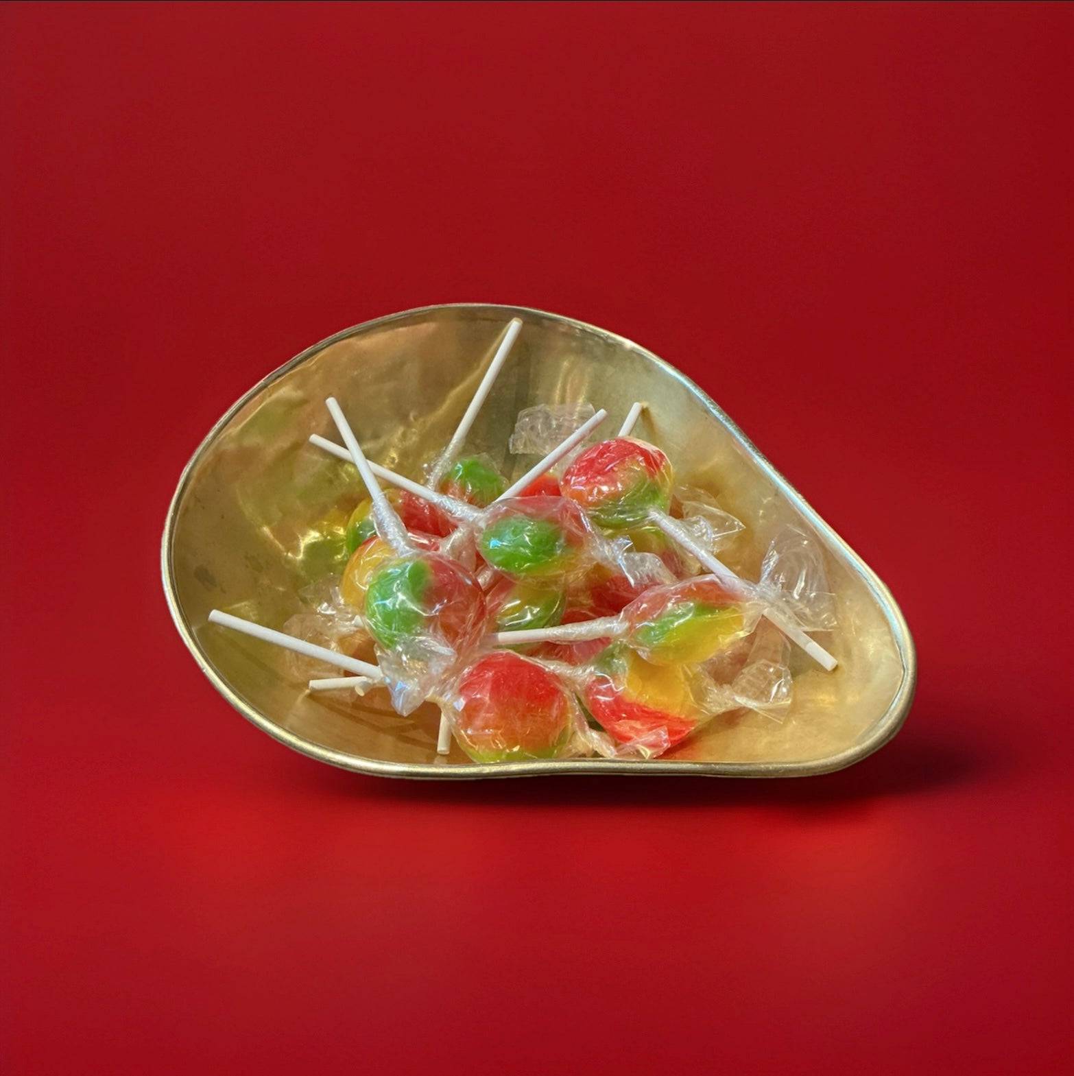 Individually wrapped hard boiled red yellow and green tropical flavoured lolly in a gold bowl on a red background 