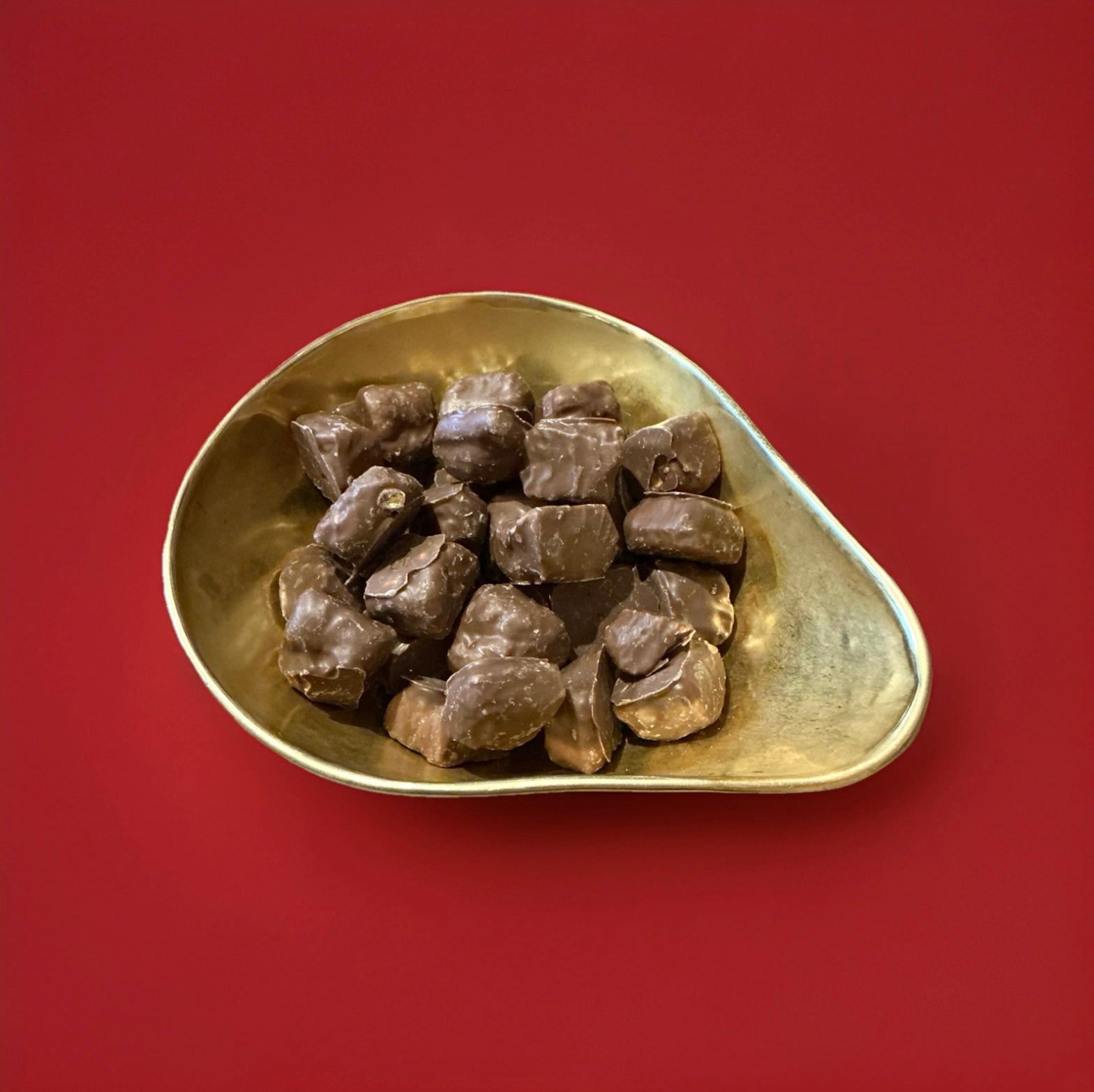 Chunks of chocolate covered cinder toffee in a gold bowl on a red background 