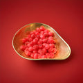Red coloured round hard boiled sweets with a cherry flavour and a fizzy sherbet centre in a gold bowl with a red background 