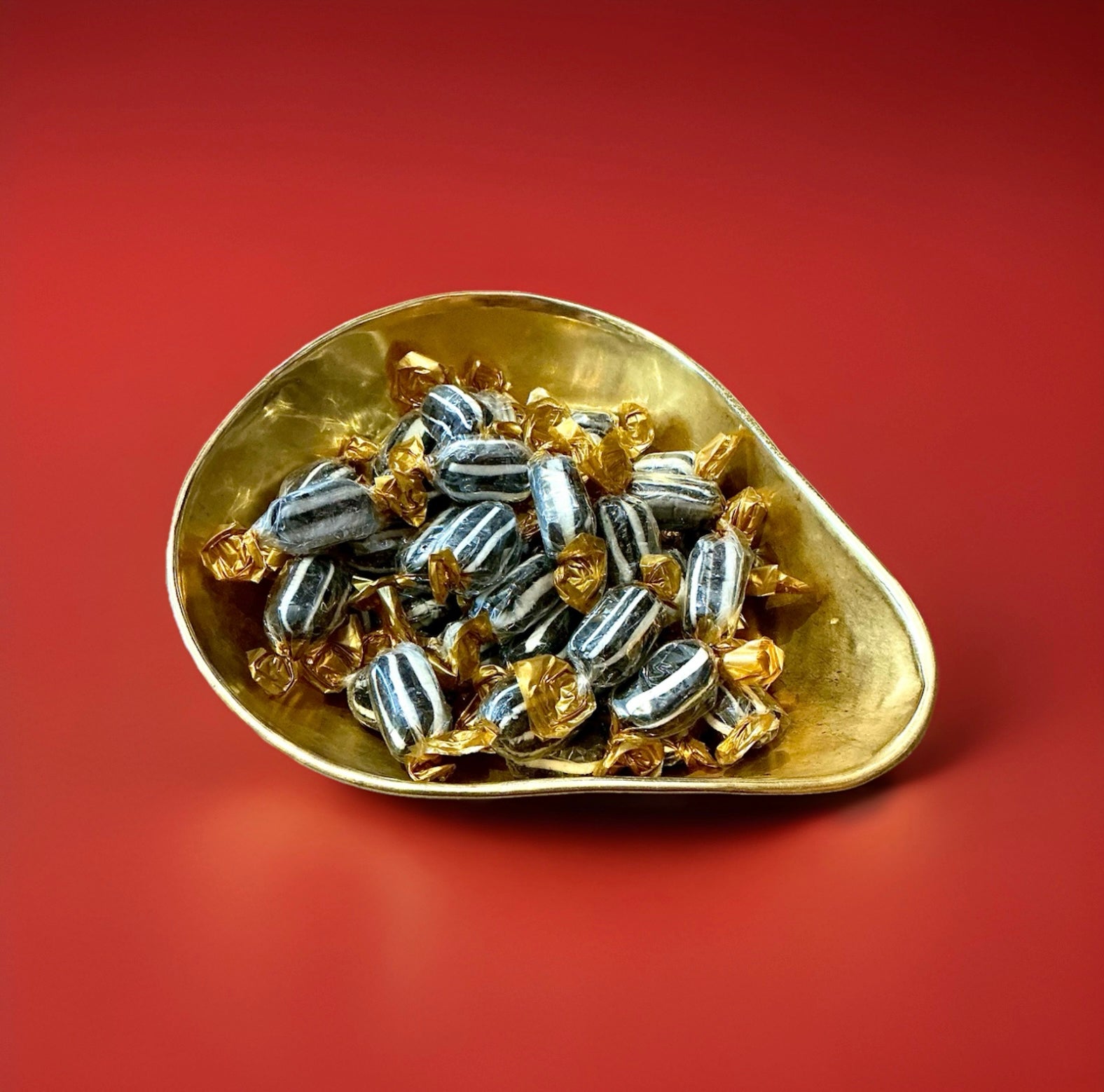 Individually wrapped black and white striped Everton mint sweets in a gold bowl on a red background 