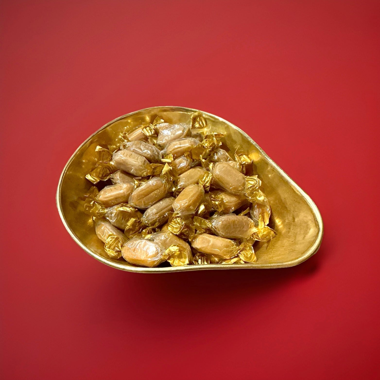 Individually wrapped brown hard boiled coffee flavoured sweets with a milk chocolate centre in a gold bowl on a red background 
