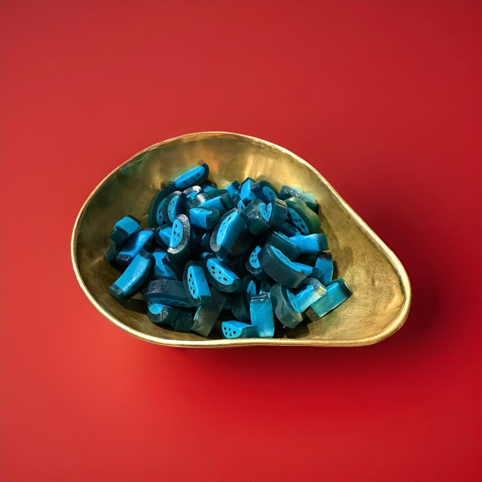 Dark and light blue raspberry flavoured sweets in a gold bowl with a red background 