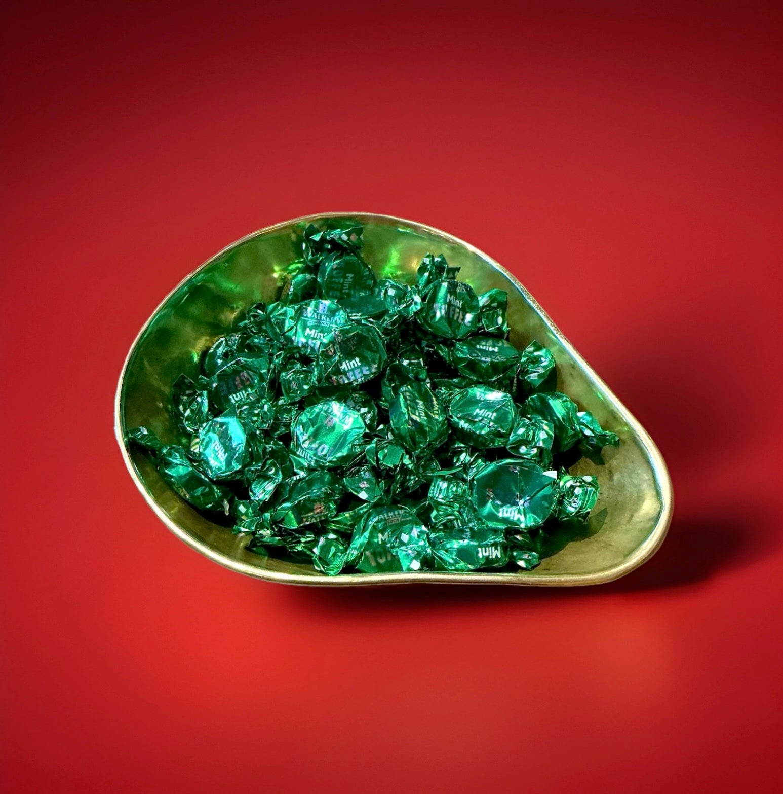 Individually wrapped green mint flavoured toffees in a gold bowl on a red background 