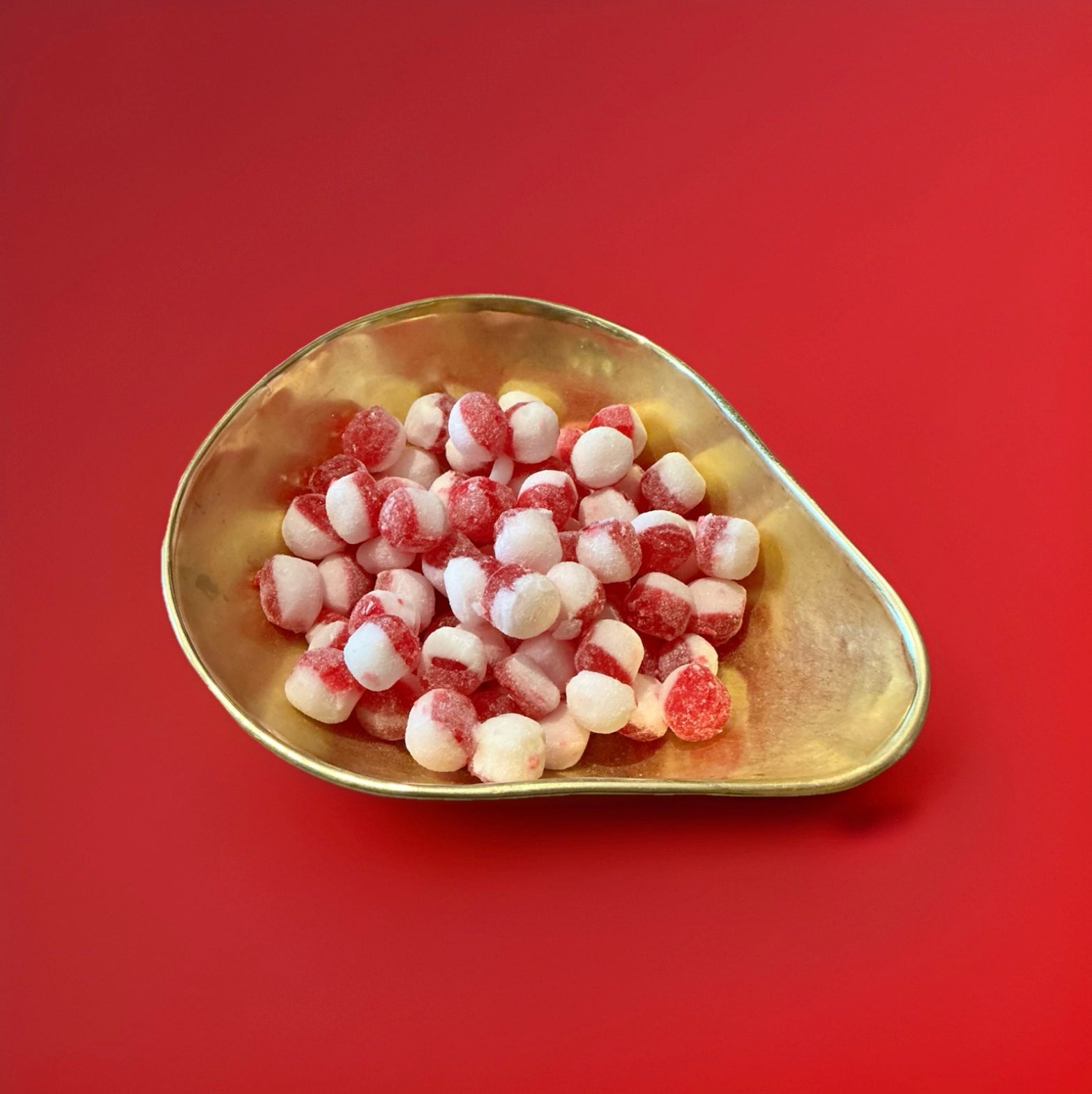 Round hard boiled red and white strawberry and cream flavoured sweets in a gold bowl on a red background 