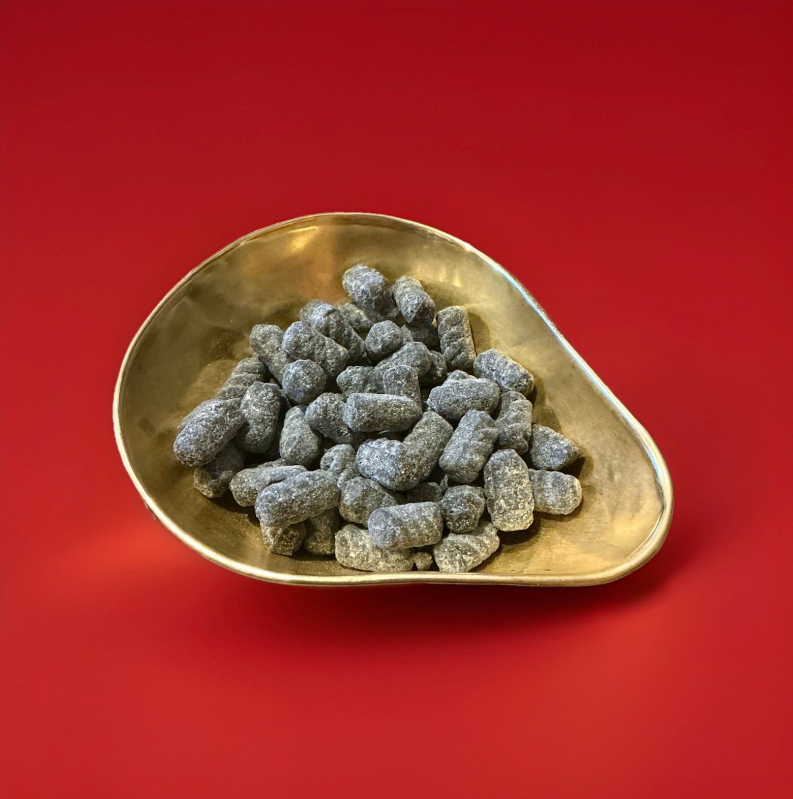 Hard boiled liquorice flavoured sweets with a sugar coating in a gold bowl on a red background 