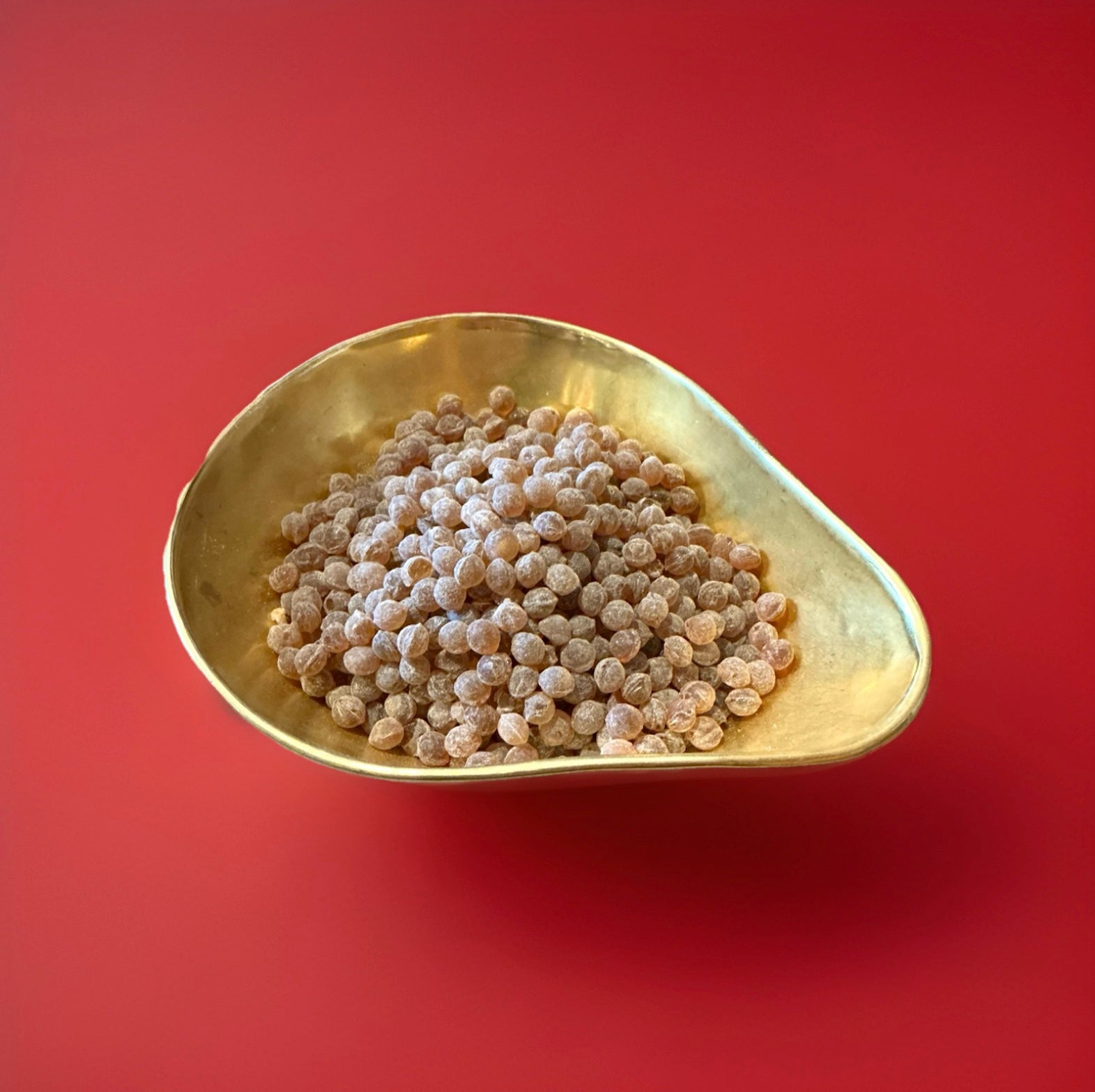Hard boiled aniseed flavoured pips in a gold bowl on a red background 