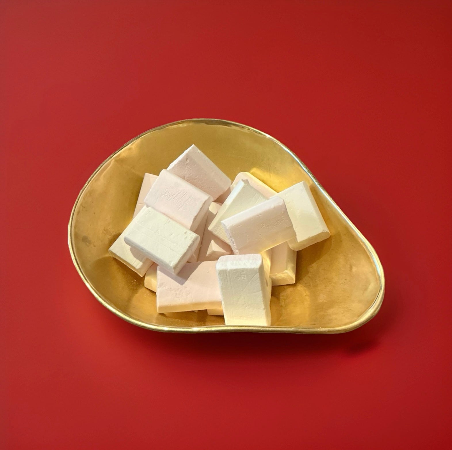 White and pink coloured strawberry flavoured sherbet blocks in a gold bowl on a red background 