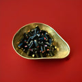 Black liquorice tubes with a white and pink fondant centre in a gold bowl on a red background 