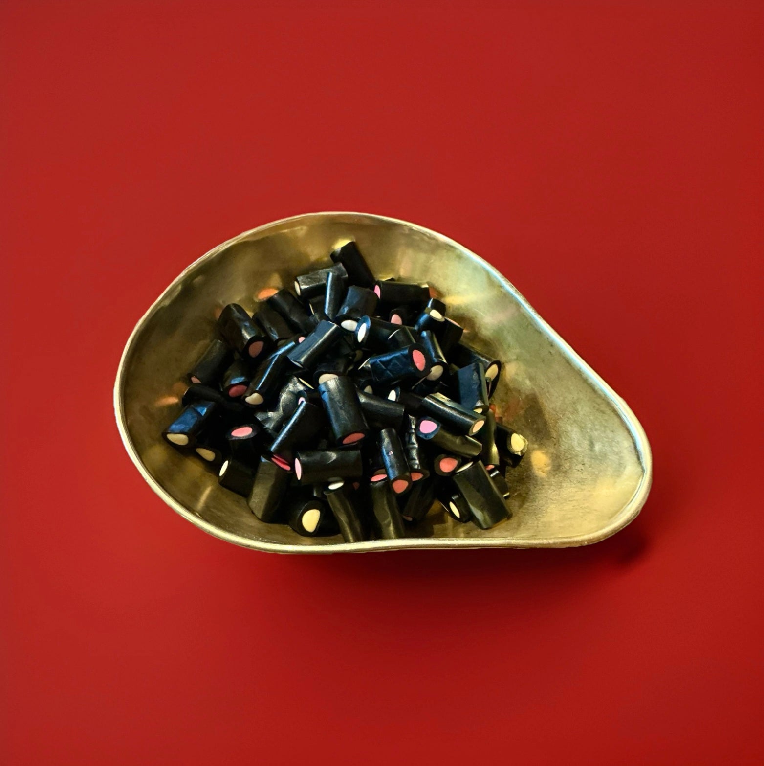 Black liquorice tubes with a white and pink fondant centre in a gold bowl on a red background 