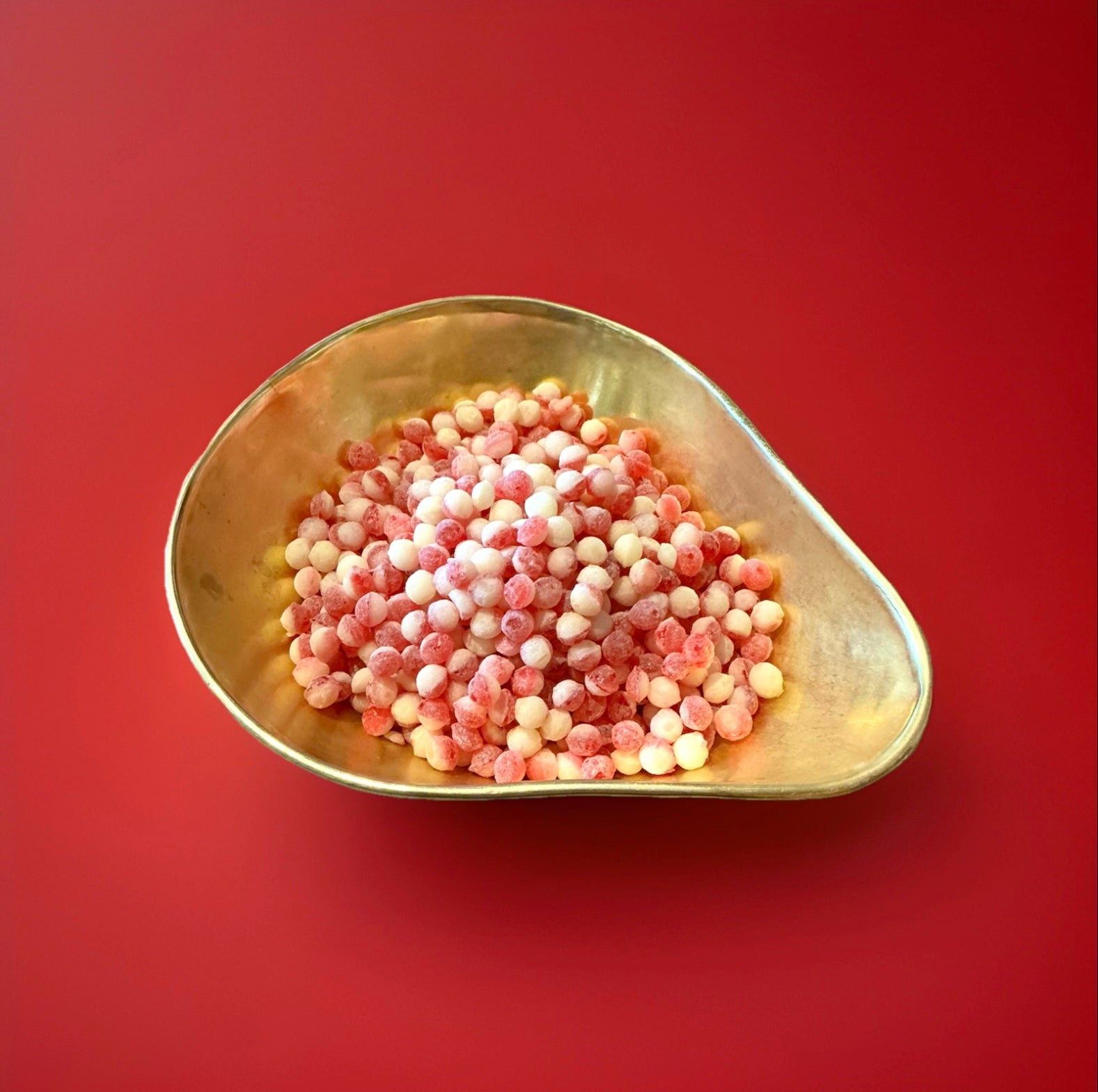 Hard boiled strawberry and cream flavoured pips in a gold bowl on a red background 