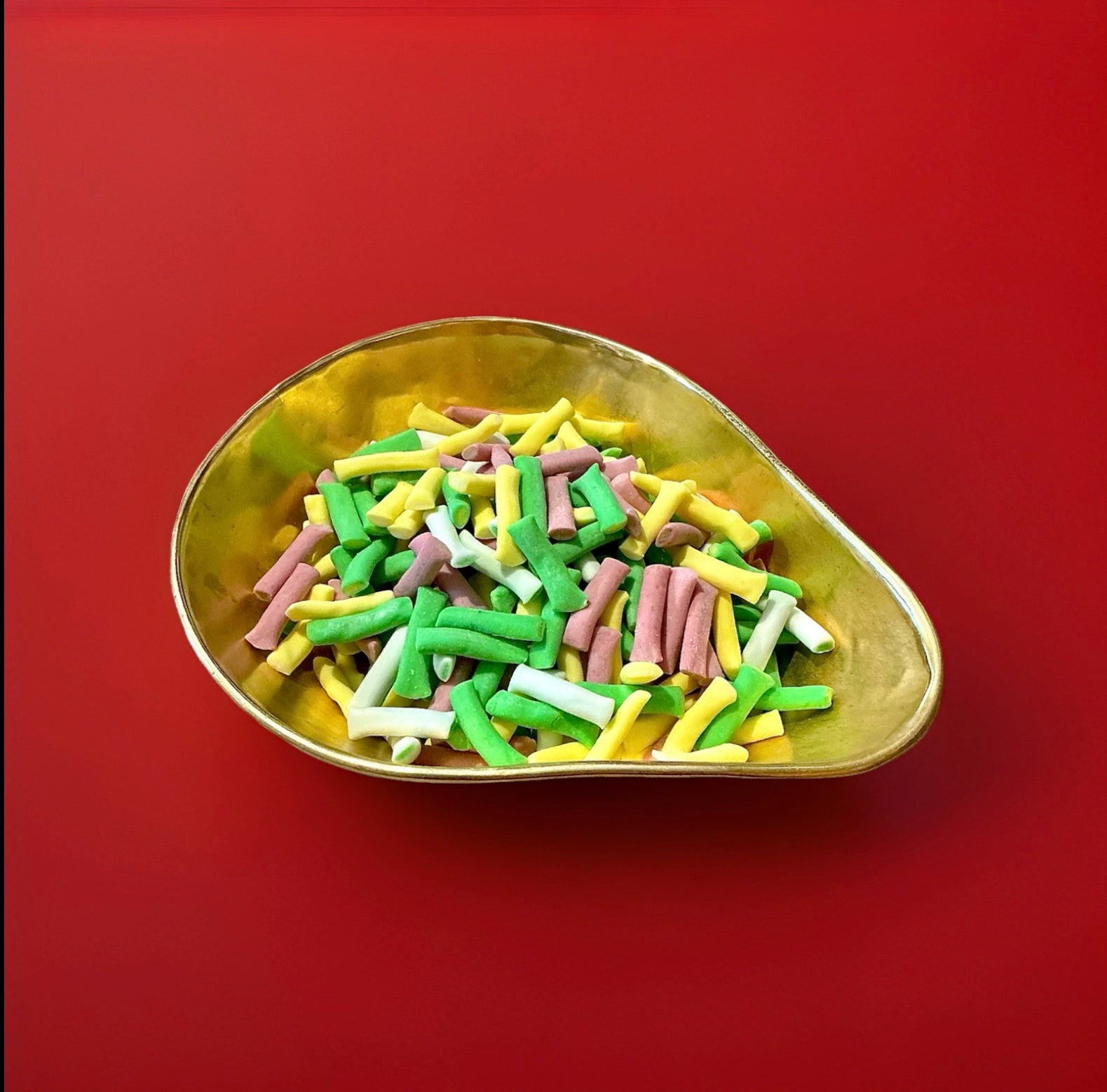 Multicoloured soft fondant rhubarb and custard tubes in a gold bowl on a red background 