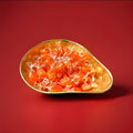 Individually wrapped orange barley sugar sweets in a gold bowl n a red background 