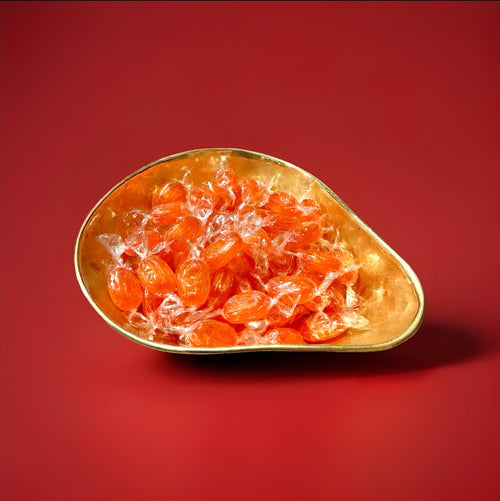 Individually wrapped orange barley sugar sweets in a gold bowl n a red background 