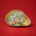 Multicoloured candy beads on an elastic necklace in a gold bowl on a red background 