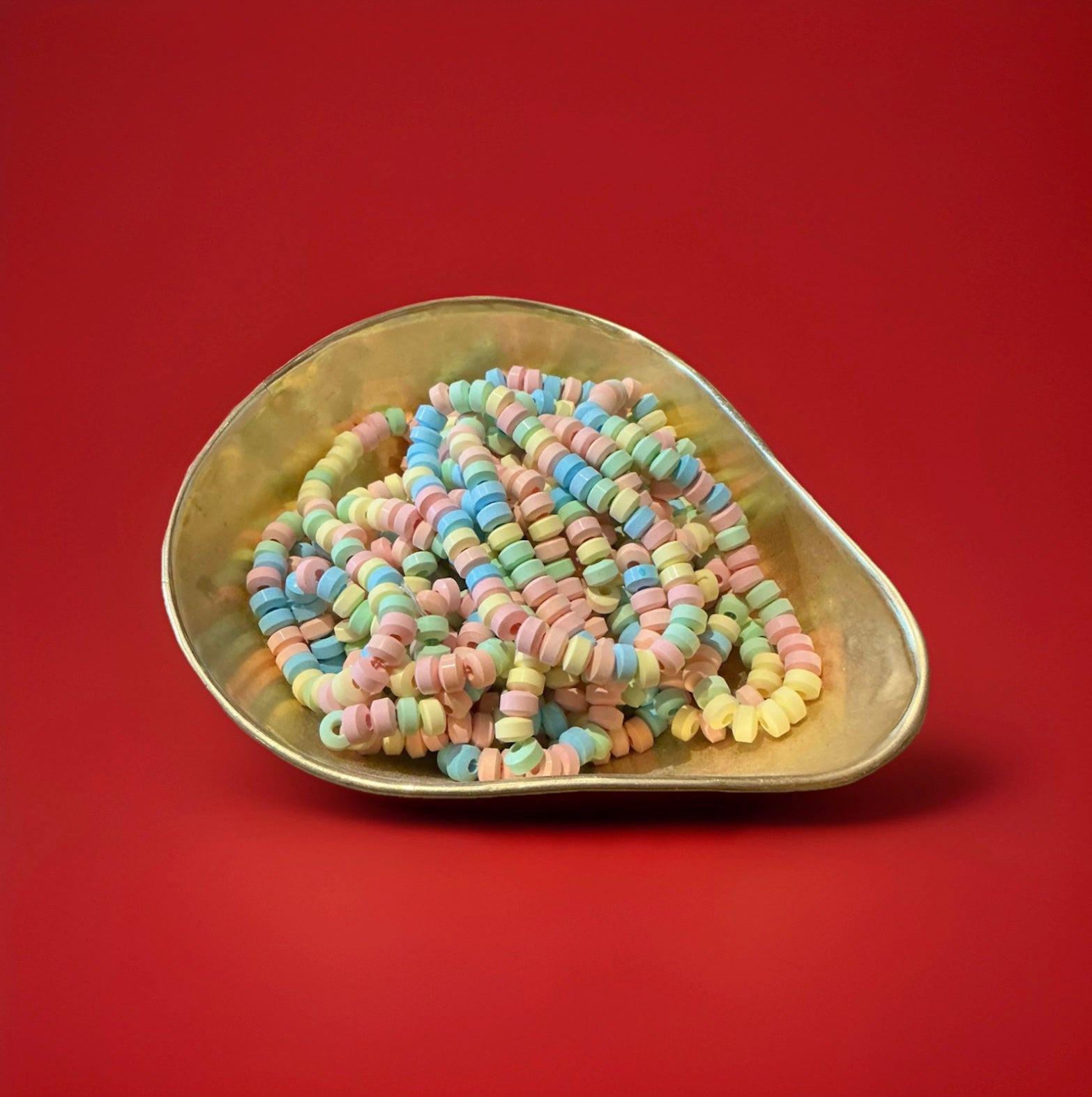 Multicoloured candy beads on an elastic necklace in a gold bowl on a red background 