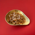 
Iight brown coloured honey and liquorice sweets shaped like honey comb in a gold bowl on a red background 