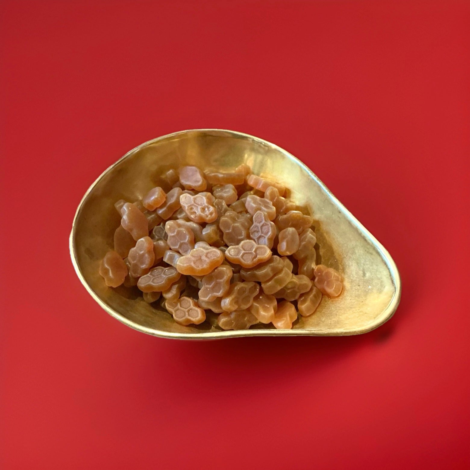 
Iight brown coloured honey and liquorice sweets shaped like honey comb in a gold bowl on a red background 