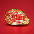 Individually wrapped red coloured aniseed twists in a gold bowl on a red background 
