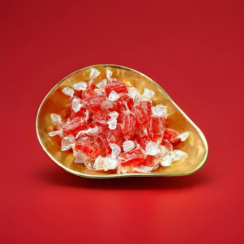 Individually wrapped red coloured aniseed twists in a gold bowl on a red background 