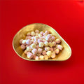 Round shaped pink and yellow coloured rhubarb and custard flavoured Bon Bon’s in a gold bowl on a red background 