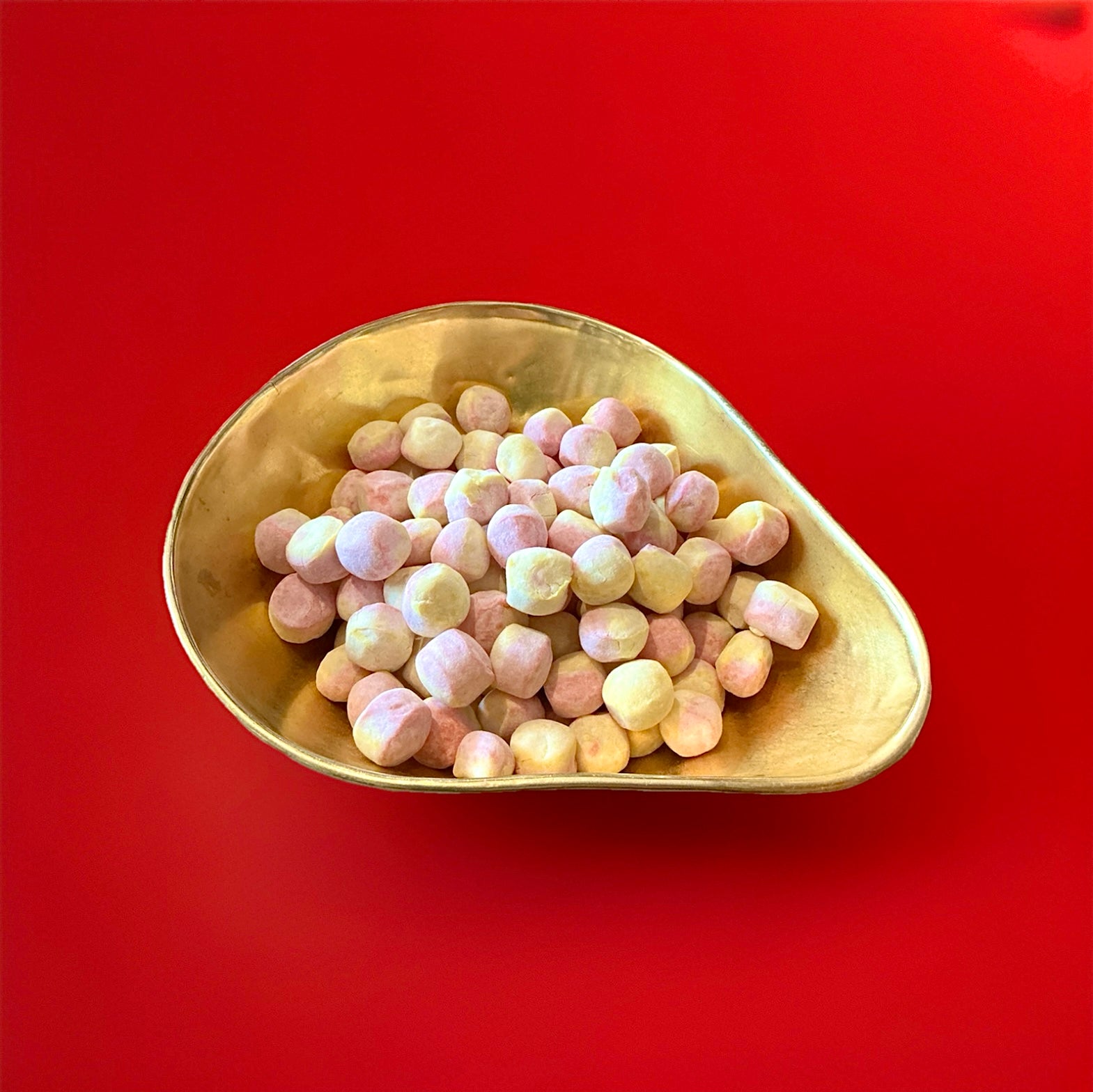 Round shaped pink and yellow coloured rhubarb and custard flavoured Bon Bon’s in a gold bowl on a red background 